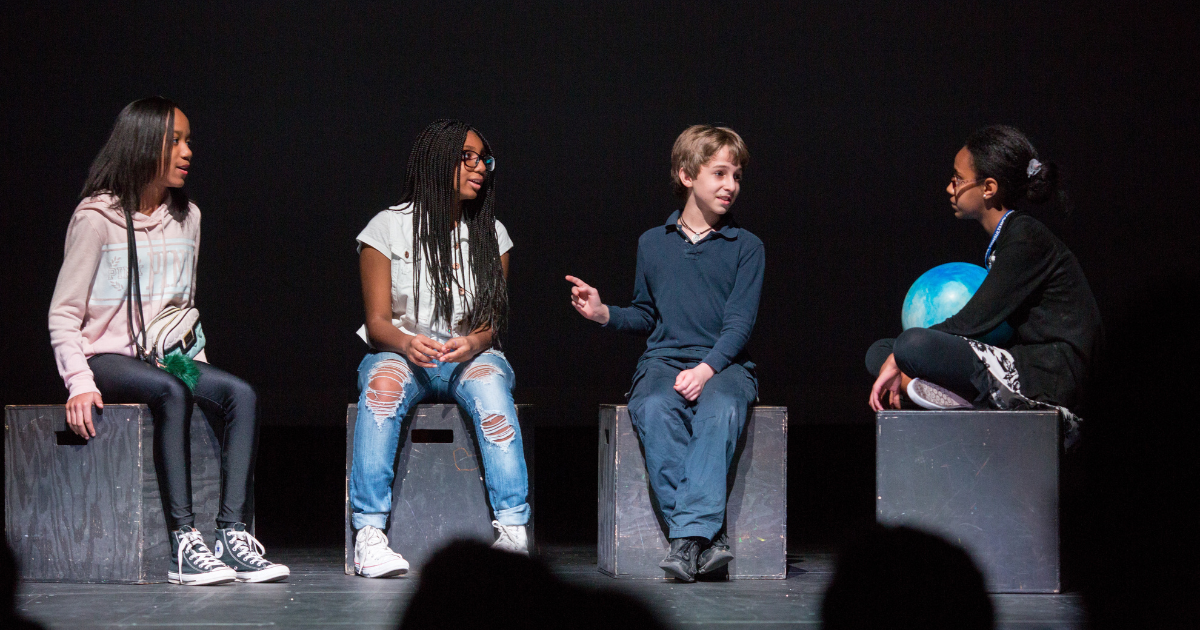 Four students on stage performing a play